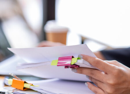 Woman sitting at desk looking through stacks of papers.