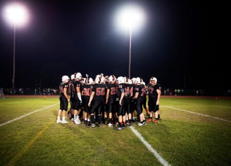 Group of high school football players standing in a huddle on a football field.